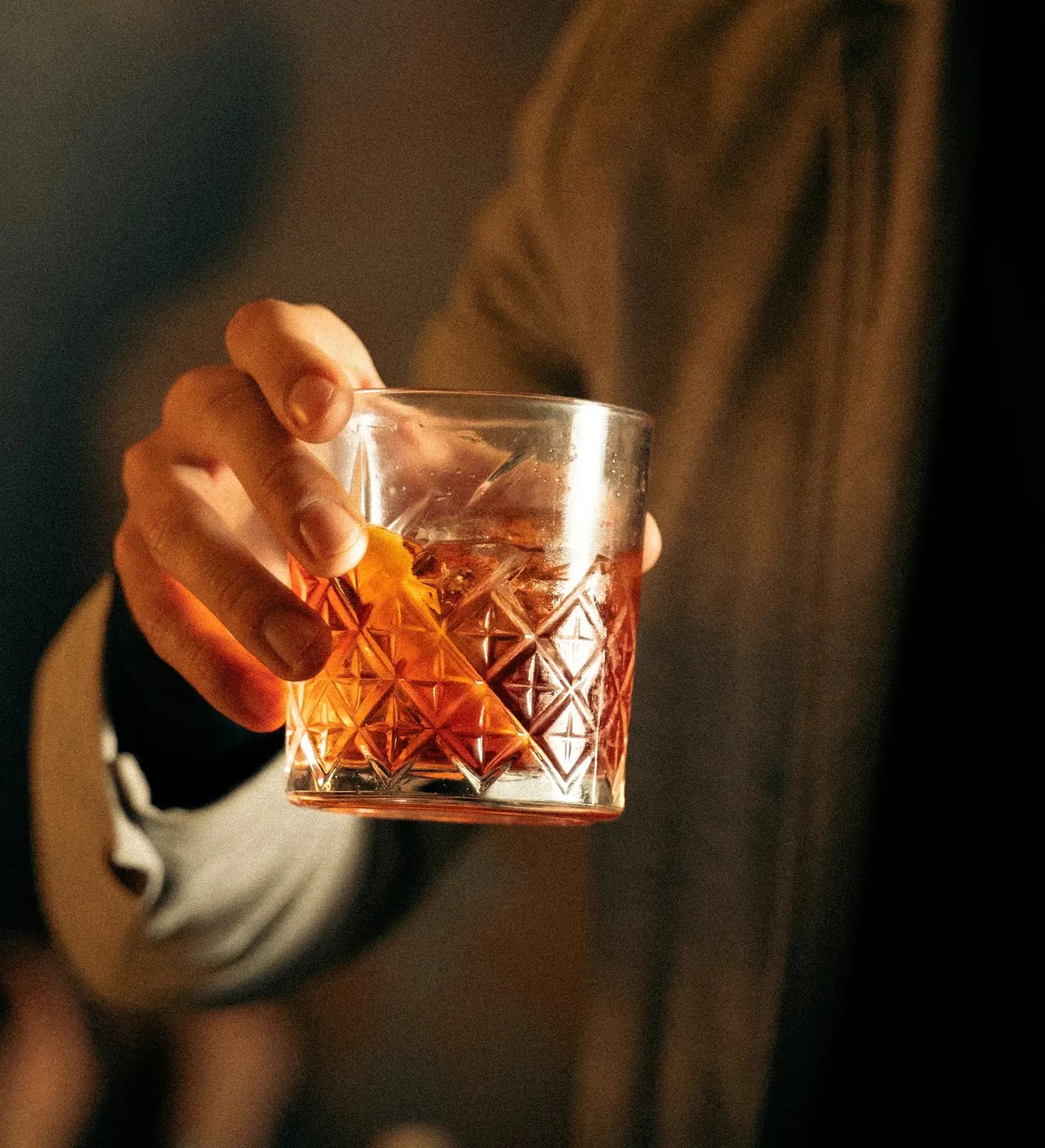 Mano che regge un bicchiere basso con rum ambrato e ghiaccio.
