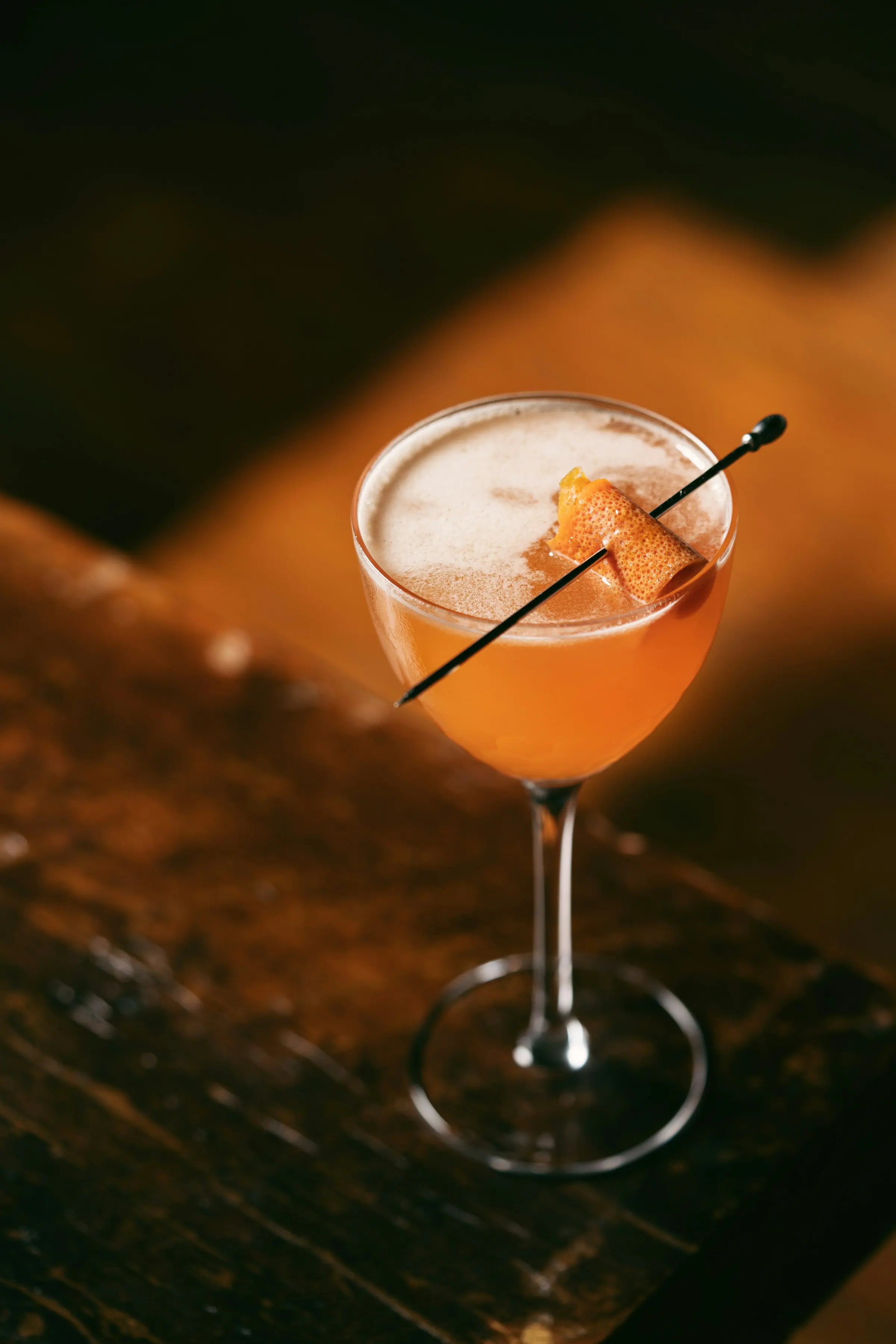 Cocktail arancione con guarnizione di agrume essiccato, in una coppa con schiuma.